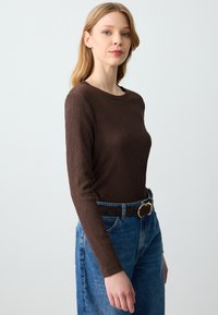 Bruine geribbelde lange mouw top met een ronde halslijn, gecombineerd met hoge blauwe jeans en een zwarte riem met een gouden gesp.