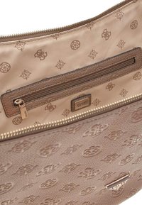 Interno della borsa a tracolla beige con una tasca con zip firmata, dettagli metallici e un motivo a logo in rilievo foderato. Chiusura a zip.