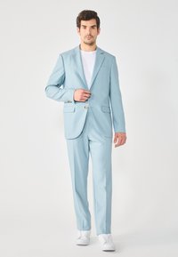 Completo azzurro chiaro con giacca monopetto, rever a punta e pantaloni su misura. Indossato con una t-shirt bianca e sneakers bianche.