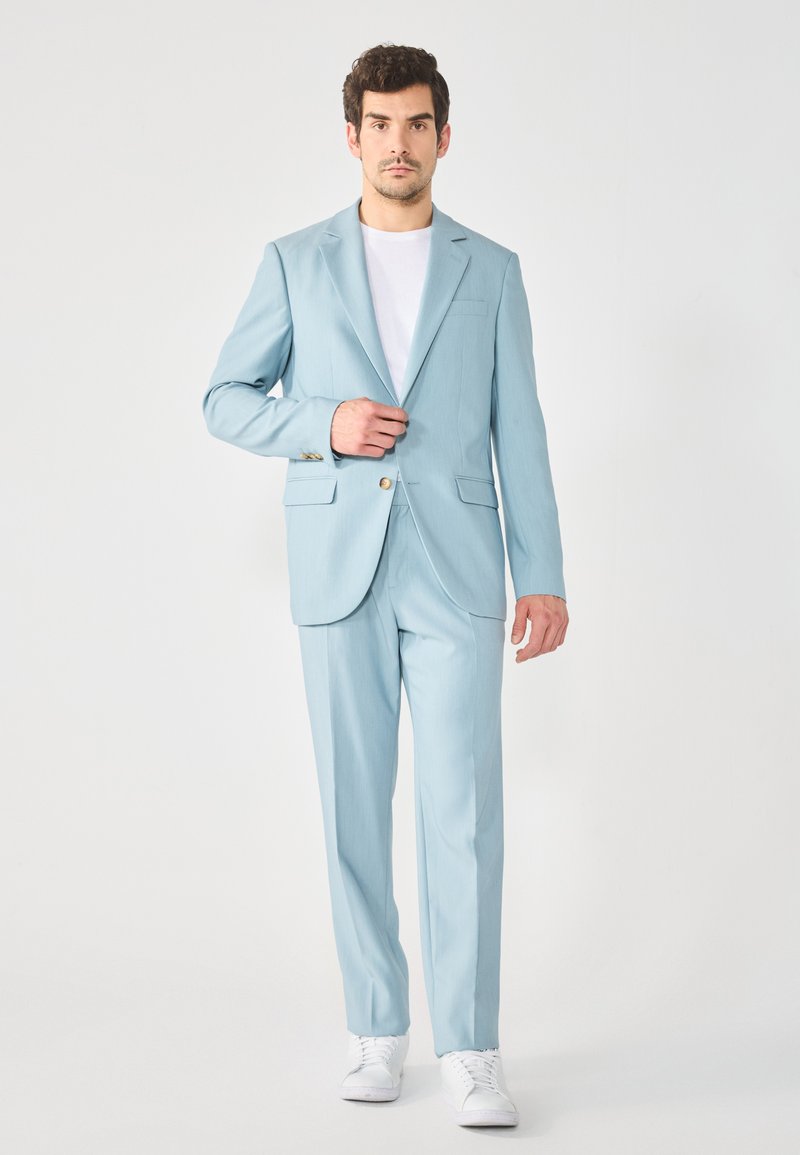 Completo azzurro chiaro con giacca monopetto, rever a punta e pantaloni su misura. Indossato con una t-shirt bianca e sneakers bianche.