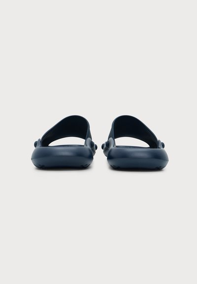 Paire de sandales slides bleu foncé à dos ouvert avec larges brides et bouts arrondis sur un fond clair uni.