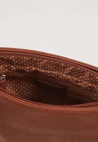 Borsa in pelle marrone con una texture liscia. L'interno presenta un motivo a pois con una tasca con zip, mostrando un design semplice.