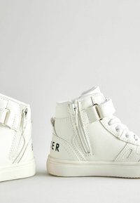 Weiße High-Top-Sneaker aus synthetischem Leder, mit einem Reißverschluss, verstellbarem Riemen und "Parker" auf der Außenseite gedruckt.