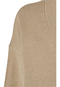 Beige knitted sweater featuring a v-neck design with a textured pattern. Soft texture with dropped shoulder seams.