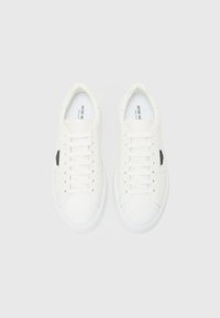 White leather sneakers with flat laces, round toe, and contrasting black logo detail on the side; smooth texture and padded collar.