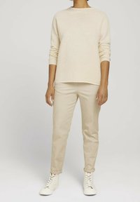 Beige gestreifter Strickpullover mit lockerer Passform, kombiniert mit hellbeigen Chinos und weißen High-Top-Sneakern. Hat lange Ärmel und einen Rundhalsausschnitt.