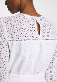 Vestido blanco de algodón bordado, con patrones de ojal, cierre de botones en la parte posterior, y una tela texturizada con una cintura fruncida.