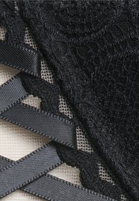 Svart blonde stoff med teksturerte mønstre, med satengbånddetaljer og meshpaneler, som skaper et lagdelt, intrikat design.