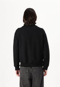 Svart sweatshirt med rund halsringning, ribbade manschetter och nedre kant, tillverkad av mjukt tyg; har raglanärmar och en slät, matt yta.