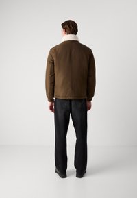 Brun polstret jakke med en hvid shearling krave, med en tætsiddende design og ribbede manchetter, parret med sorte jeans.