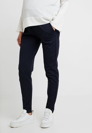 Marineblaue Stretchhosen mit Seitentaschen, schmaler Passform und glatter Textur. Kombiniert mit weißen Sneakers mit profiliertem Sohlenmuster und Schnürsenkeln.