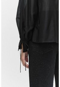 Svart, lätt blus med puffärmar och knytningar vid ärmsluten, kombinerad med svarta denimjeans med små nitar.