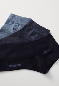 Tri parova čarapa Calvin Klein u raznim nijansama plave: svijetloplava, tamnoplava i mornarska. Svaka sadrži mali "ck" logo i glatku teksturu.