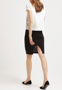 Hvid cropped t-shirt med korte ærmer, som har et mønstret ryg, parret med en tætsiddende sort ribbet nederdel med slids i siden.