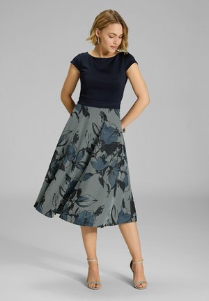 Haut à manches courtes bleu marine associé à une jupe A-line à motifs floraux en rayures bleu, noir et blanc, avec une taille ajustée et une coupe fluide.