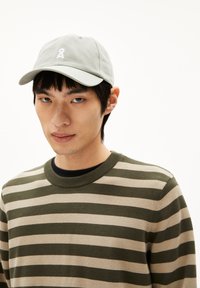 Lichtgrijze baseballcap met een logo op de voorkant, gecombineerd met een groen en beige gestreepte trui, ronde hals en geribde manchetten.