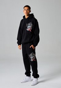 Conjunto de sudadera y pantalones negros con diseños gráficos, que presenta motivos de dragones y llamas coloridas. Combinado con zapatillas blancas.