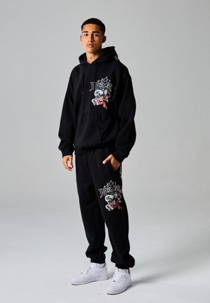 Black sweatshirt and pants set with graphic designs, featuring colorful dragon and flame motifs. Paired with white sneakers.