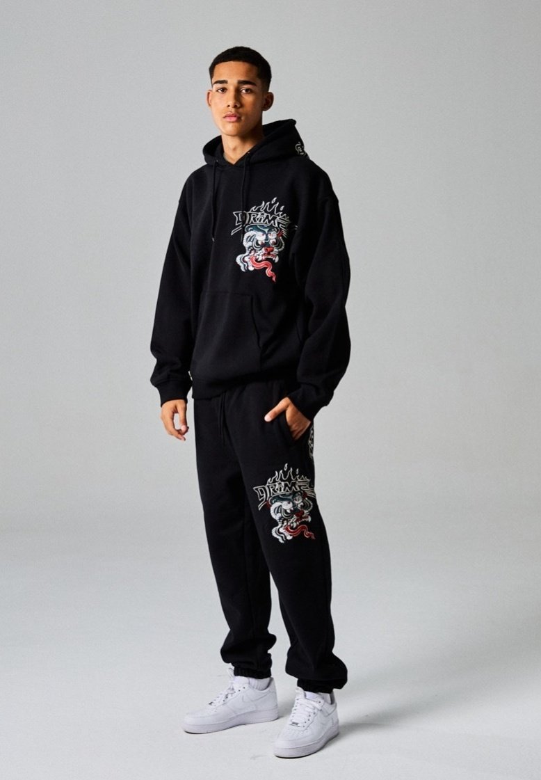 Conjunto de sudadera y pantalones negros con diseños gráficos, que presenta motivos de dragones y llamas coloridas. Combinado con zapatillas blancas.