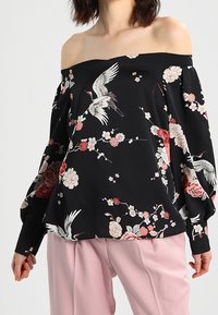 Czarna bluzka bez ramiączek z kwiatowym i żurawim nadrukiem. Posiada luźne rękawy i swobodny krój, wykonana z gładkiego materiału.