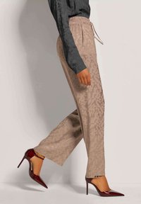 Beige weite Hosen mit einem dezenten Tiermuster, elastischem Bund und Kordelzug, kombiniert mit glänzenden burgunderfarbenen Stilettos.