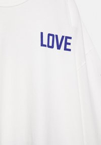 White fabric with bold blue text "LOVE" printed on the upper left side, showing part of a long-sleeve garment.