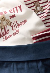 Bawełniana bluza z grafiką misia i tekstem w kolorze bordowym. Czerwono-biały, paskowany dekolt. Niebieski dół bluzy z prążkowanym ściągaczem.