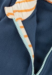 Marineblaue Fleece-Jacke mit mintgrünem Reißverschluss und gestreiftem Baumwollfutter in Orange und Creme. Glatte Textur und schräges Öffnungsdesign.