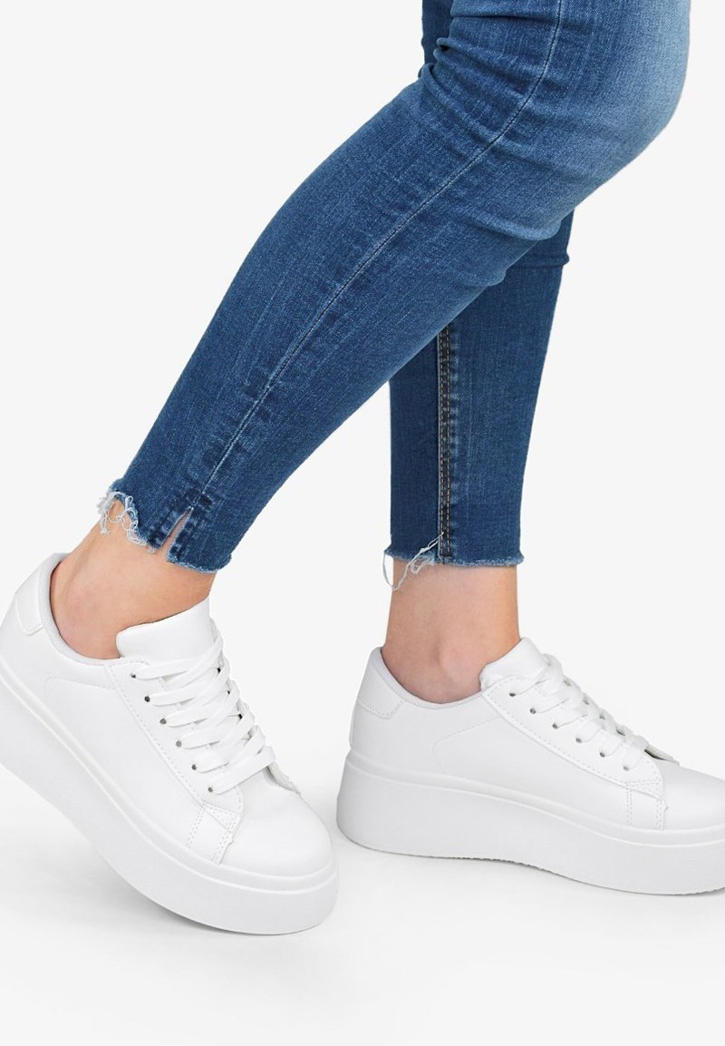 Sneaker platform bianche con tomaia in pelle liscia, punta rotonda e lacci. Abbinate a jeans skinny blu scuro con orli sfilacciati.