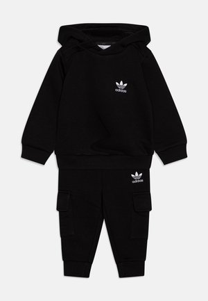 Ensemble composé d'un sweat à capuche noir et d'un pantalon cargo en tissu doux. Présente le logo blanc d'Adidas sur les deux pièces. Le hoodie dispose d'un cordon de serrage et d'une poche kangourou.