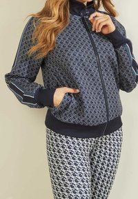 Jacket blu navy con zip e motivo logo ripetuto, polsini e colletto a coste; abbinato a leggings coordinati con design e schema di colori simili.