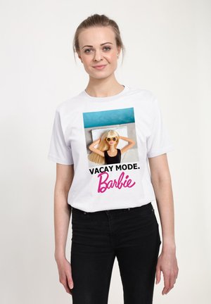 T-shirt bianca con una grafica di una bambola Barbie con occhiali da sole, con il testo "VACAY MODE." in nero e rosa. La maglietta ha una vestibilità rilassata.