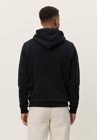 Μαύρο φούτερ με κουκούλα και απαλό ύφασμα, με ραβδωτά μανσέτες και μέση. Διαθέτει ευρύχωρη πίσω τσέπη και απλό σχέδιο χωρίς μοτίβα.