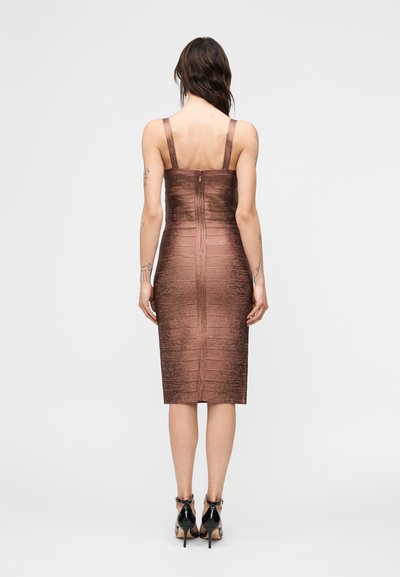 Γυναίκα που φοράει εφαρμοστό, μαν sleeveless, μεταλλικό καφέ midi φόρεμα με φερμουάρ στο πίσω μέρος, στέκεται με την πλάτη στην κάμερα σε απλό φόντο.