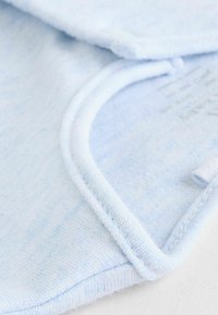 Tissu bleu clair avec une texture douce et des détails de couture, présentant un col rond et une étiquette partiellement visible.