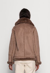 Brun shearlingjacka med en mjuk pälskrage, som har en avslappnad passform, sömdetaljer och ärmar och nederkant med päls. 