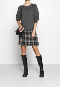 Pull en tricot gris à manches dolman associé à une jupe plissée à carreaux noir et blanc. Bottes noires à talons hauts jusqu'au genou et un petit sac noir.