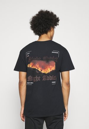 T-shirt en coton noir avec un imprimé graphique au dos représentant des flammes, le texte "Night Addict" et des détails d'interface de caméra. Manches courtes.
