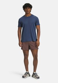 T-shirt de sport bleu marine à manches courtes, avec des détails de ventilation texturés. Associé à un short marron et des chaussures de course multicolores.
