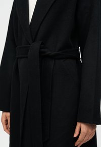 Μαύρο μάλλινο παλτό με γιακά σάλι, ζώνη στη μέση και πλαϊνές τσέπες. Διαθέτει απαλό, υφασμάτινο ύφ ασμα με υφή και μακριά μανίκια.