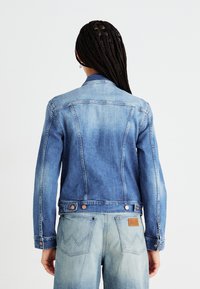 Jasnoniebieska kurtka dżinsowa o wyblakłym wyglądzie, z długimi rękawami i mosiężnymi guzikami. Para jasnoniebieskich dżinsów z widocznymi tylnymi kieszeniami.