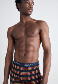 GANT Herren Boxershorts in Marineblau mit roten und gelben Streifen, ausgestattet mit einem schwarzen elastischen Bund mit weißer Logo-Schrift. Glatte Stoffstruktur.