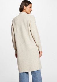 Beige lång cardigan med avslappnad passform, ribbade muddar och en slät textur, i kombination med ljusblå vida jeans.