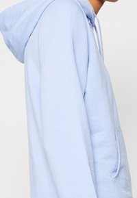 Sudadera con capucha azul claro con bolsillo canguro, capucha con cordón, textura de tela suave y puños acanalados, vista desde un lado.