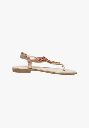 Person trägt rotes Kleid und Sandalen mit roten und goldenen verzierten Riemen und steht neben einem Auto auf Beton.