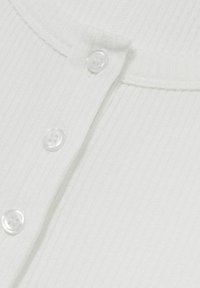 Weißer gerippter Pullover mit runder Ausschnittform und vier transparenten Kunststoffknöpfen entlang der Vorderseite. Weicher Stoff und taillierte Passform.