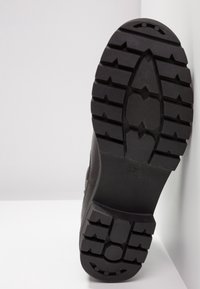 Zwarte rubberen zool met diepe profiel, voorzien van een ovale center en hoekige patronen. Maat aangeduid als 37. Achtergrond is neutraal en eenvoudig.