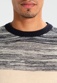 Gebreide trui met een ronde marineblauwe halslijn, een gestructureerd gestreept patroon in marineblauw en crème, en een gladde crème onderkant.