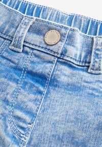 Ljusblå denimjeans med knappstängning och sydda detaljer. Tyget har en blekt textur och en rund metallösning som accenterar midjebandet.
