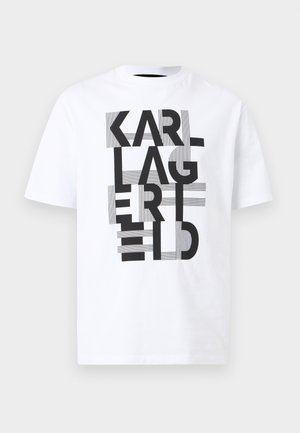 Hvit t-skjorte med korte ermer og fet svart tekst "KARL LAGERFELD" arrangert vertikalt med horisontale stripete aksenter på en ensfarget bakgrunn.